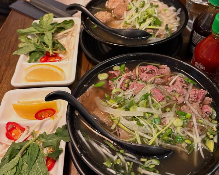 Two bowls of pho with fresh herbs and dipping sauces at Hoa Sen