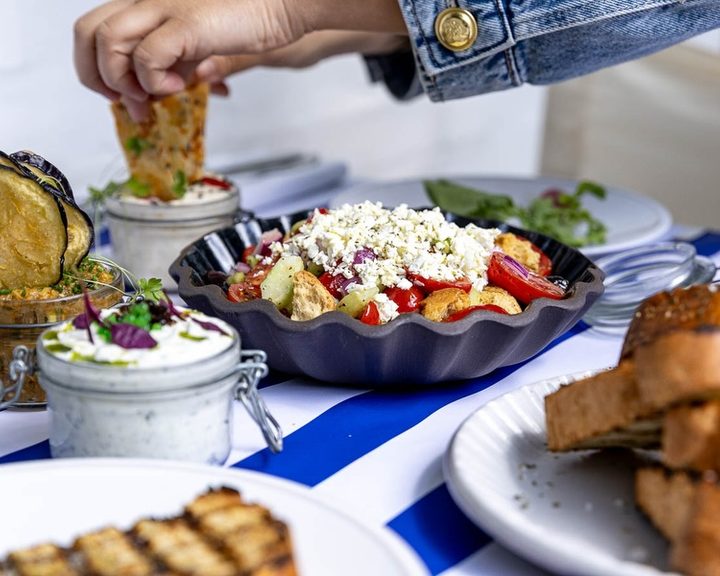 Greek salad, jars of dips and bread on a table at Mazi in Notting Hill